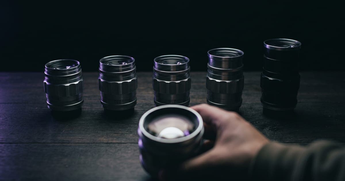 Five camera lenses of different focal lengths in a row, one picked up in the foreground.