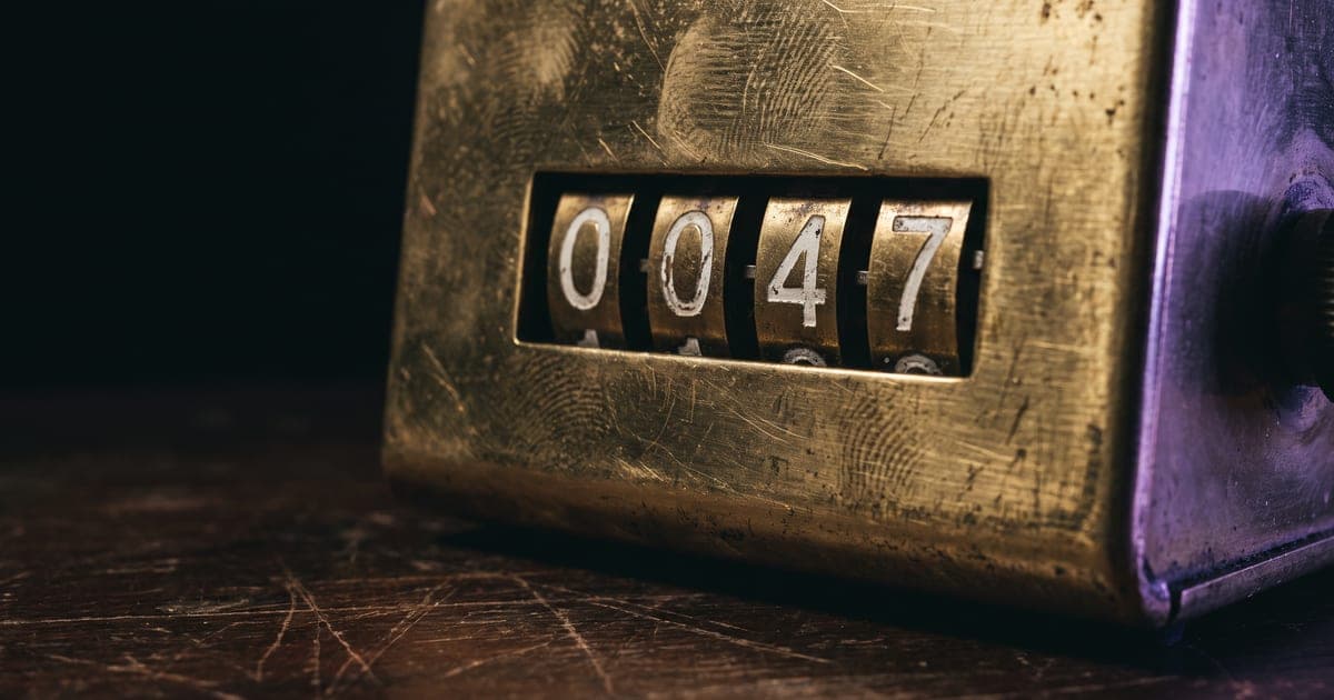 A brass mechanical counter on a dark desk, its number wheels catching a hard light.