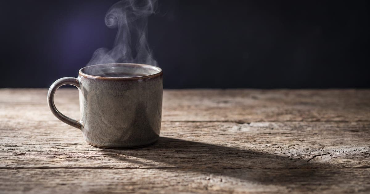 A ceramic mug on an oak table, lit from one side, the background falling out of focus.