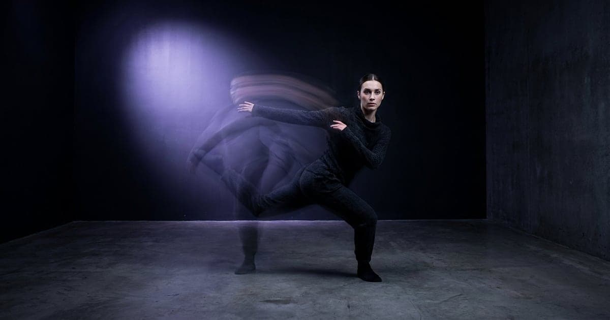 A dancer mid-move in an empty white studio, motion trails behind the arms.