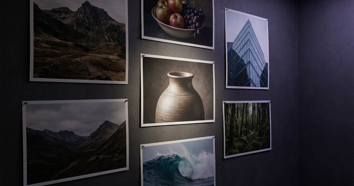 Large photographic prints of landscapes and objects pinned on a dark studio wall, one in the centre lit.