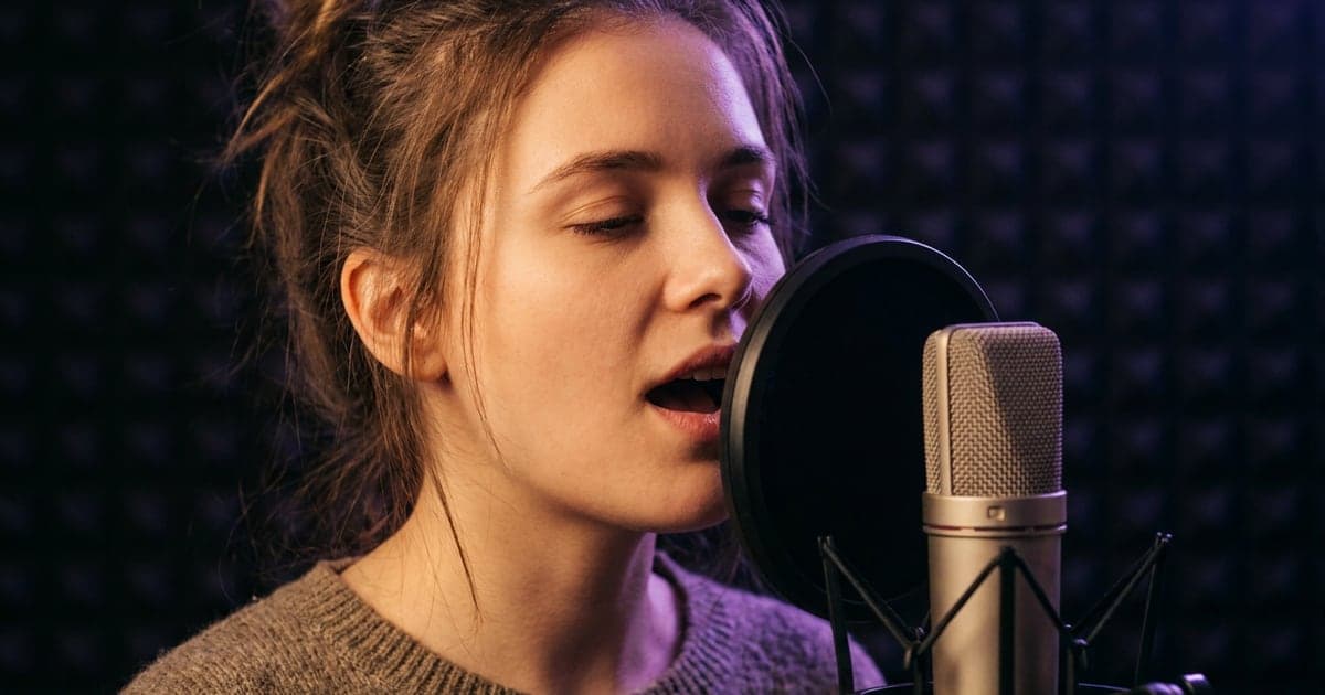 Close-up of a singer at a studio microphone mid-word, mouth open on a vowel.