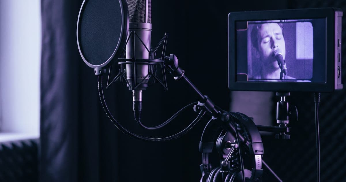 A studio microphone with a pop filter in front of a small monitor showing a film frame, purple light.