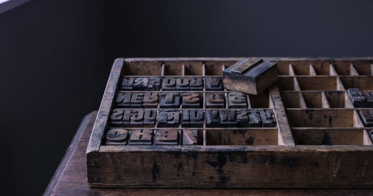 A drawer of printing blocks, one lifted out and held above the rest.