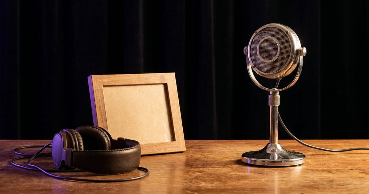 A vintage studio microphone on a wooden desk beside an empty picture frame and headphones, warm light.