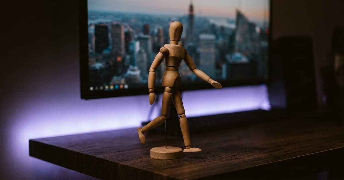 A small wooden artist mannequin posed mid-step in front of a large screen showing a street scene.