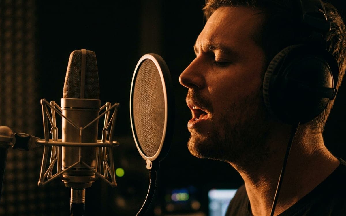 A singer at a microphone in a dark studio, mid-word, lit from the side.